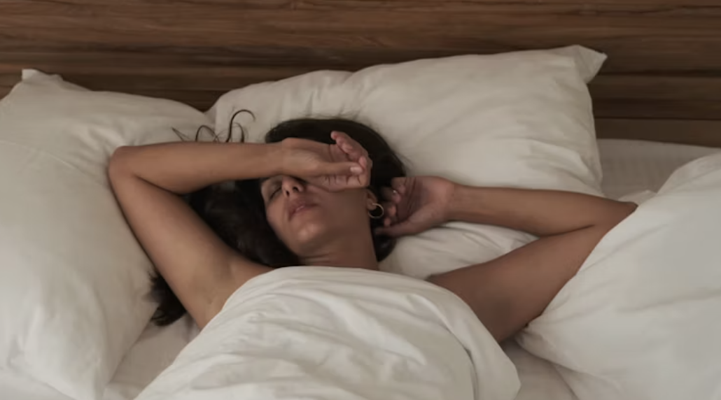 A woman lying in bed, an arm across her eyes, exhausted